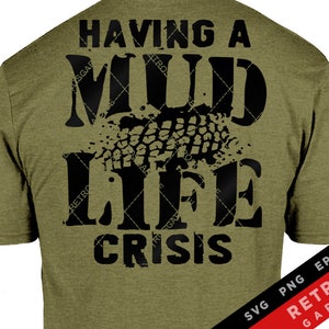 以下が含まれることがあります： 黒い文字で「Having a Mild Life Crisis」と書かれた緑色のTシャツ。文字の上に黒いタイヤのトレッドパターンが重ねられています。Tシャツの右下には赤い文字で「SVG PNG EPS AI RETROS GARAGE」と書かれています。