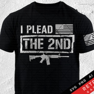 Op de afbeelding: Zwart T-shirt met een witte afbeelding waarop "I Plead The 2nd" staat met een Amerikaanse vlag en een silhouet van een geweer. Het shirt heeft ook een kleine Amerikaanse vlag op de mouw.