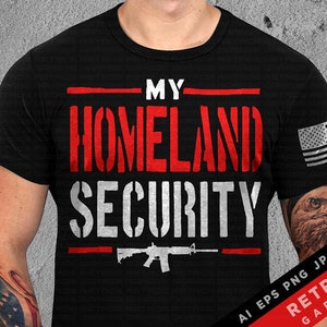 May include: Black t-shirt with the text "MY HOMELAND SECURITY" in red and white, featuring a rifle graphic. An American flag is on the sleeve. The shirt is a classic crew neck.