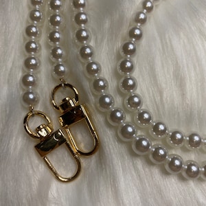 May include: A white pearl chain with two gold clasps. The chain is made of faux pearls and is perfect for adding a touch of elegance to any outfit.