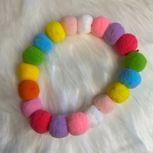 May include: A colorful garland of pom-poms in various shades of pink, red, orange, yellow, green, blue, and purple.