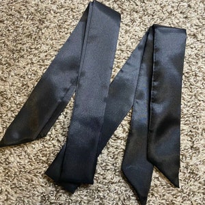 May include: Three black satin ribbon ties. The ribbons are long and narrow, with a smooth, silky texture.