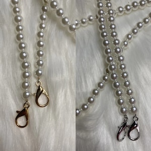 May include: Two white pearl necklaces with gold and silver clasps. The necklaces are on a white fuzzy surface.