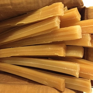 May include: A box filled with multiple long, thin bars of light brown soap. The soap bars are stacked on top of each other and are arranged in a random pattern.