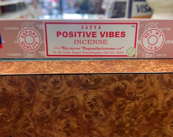 May include: A pink and white box with the text "SATYA POSITIVE VIBES INCENSE" and the text "Mirs. Shrinivas "Sugandhalaya(BNG) LLP™ 1/9, 8th Cross, Magadi Road, Bengaluru-560 023, INDIA" printed on it.