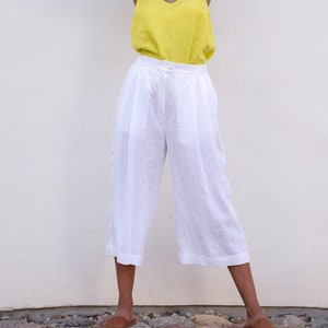 Woman in yellow top and white elastic waist linen culottes posing against a plain wall, embodying summer chic.