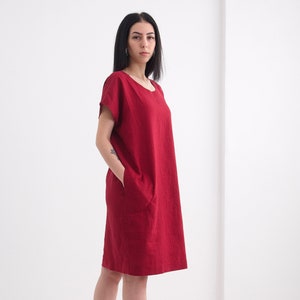 Puede incluir: Un vestido de lino rojo con mangas cortas y cuello redondo. El vestido tiene un corte holgado y llega a la mitad del muslo.