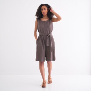 Peut inclure: Une femme portant une combinaison en lin marron avec une large ceinture. Elle est debout sur un fond blanc et a les cheveux tir&eacute;s en arri&egrave;re.