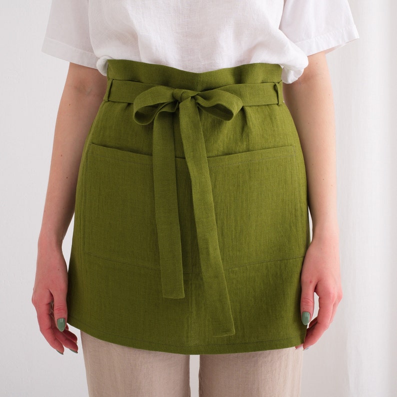 A woman wearing a stylish green linen apron skirt made from premium European high-quality linen, available by the yard from a specialized linen fabric store.