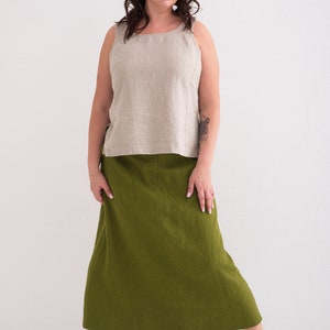 A woman models a casual outfit featuring a natural linen tank top and a green linen skirt, paired with white sneakers.