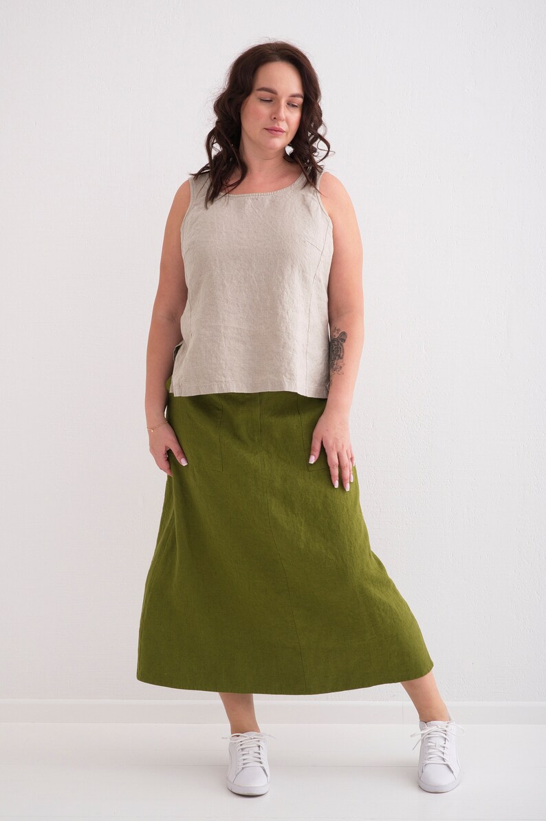 A woman models a casual outfit featuring a natural linen tank top and a green linen skirt, paired with white sneakers.