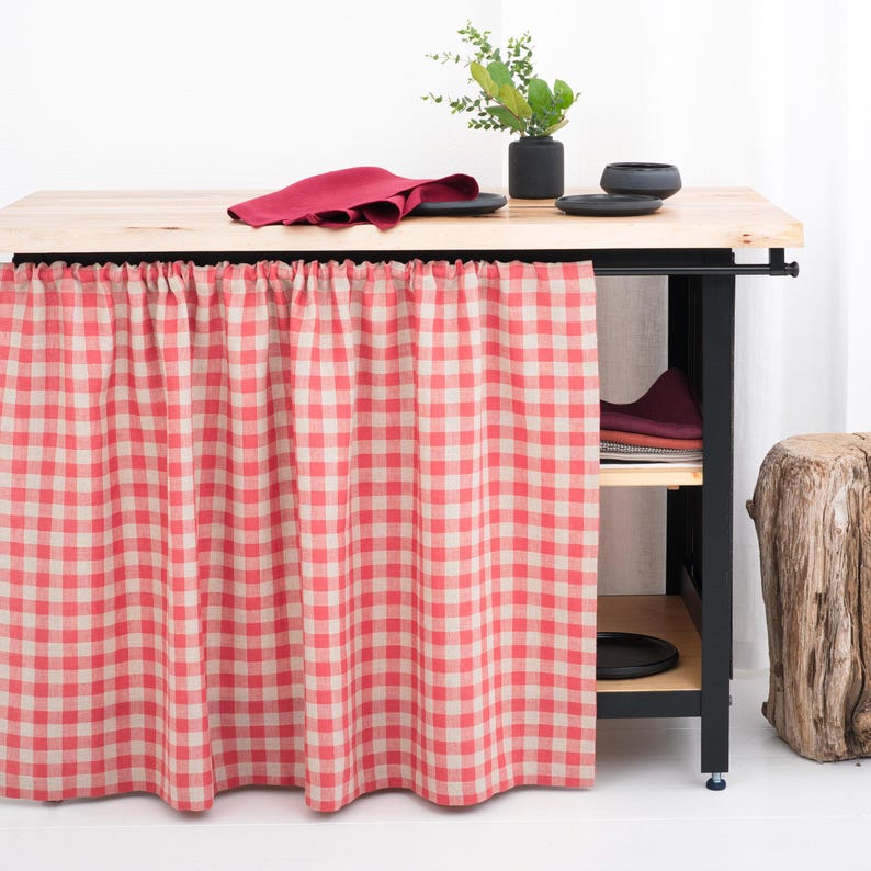 Red gingham cafe curtains with a classic check pattern brighten a farmhouse-style kitchen window. Cheerful and vintage-inspired