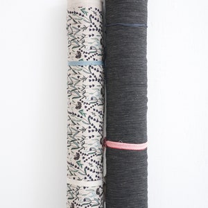 Rolls of striped linen fabric and floral prints, showcasing premium European quality flax textiles in natural offwhite and wide striped patterns, available for sale by the yard.