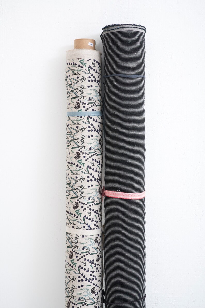 Rolls of striped linen fabric and floral prints, showcasing premium European quality flax textiles in natural offwhite and wide striped patterns, available for sale by the yard.