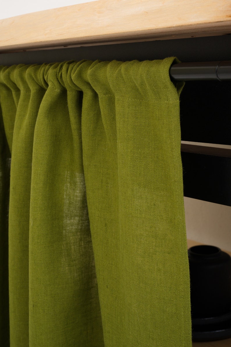 Close-up of moss green stone washed linen privacy curtain with gathered top, against a wooden shelf.