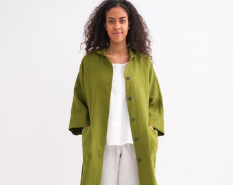 May include: A long, green linen jacket with a hood and pockets. The jacket has a button closure and is worn over a white shirt and white pants.