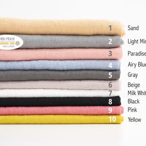 Puede incluir: Una pila de diez muestras de tela de lino en varios colores, incluyendo arena, menta clara, melocot&oacute;n para&iacute;so, azul claro, gris, beige, blanco leche, negro, rosa y amarillo. Las muestras est&aacute;n etiquetadas con n&uacute;meros y nombres de colores. Se ve una etiqueta OEKO-TEX Standard 100.