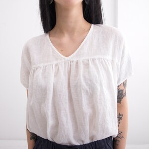 May include: A white linen blouse with a v-neck and a gathered bodice.