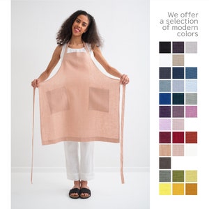 "A joyful woman displaying a natural linen plus size apron in peach, perfect for gardening with spacious pockets."