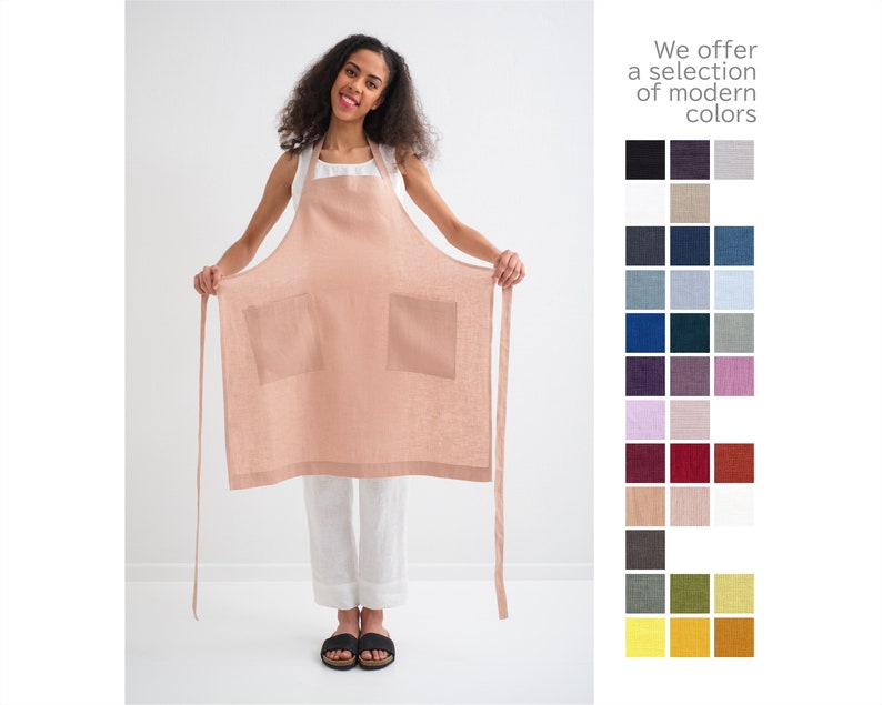 "A joyful woman displaying a natural linen plus size apron in peach, perfect for gardening with spacious pockets."