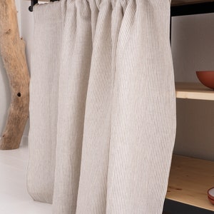 May include: A pair of white linen curtains with thin brown stripes hanging from a wooden rod. The curtains are gathered at the top and hang straight down.