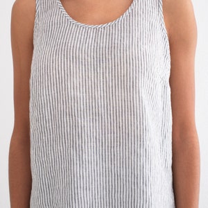 Puede incluir: Camiseta sin mangas con rayas verticales grises y blancas. La parte superior tiene un cuello redondo y est&aacute; hecha de una tela ligera. La prenda forma parte de un conjunto a juego.