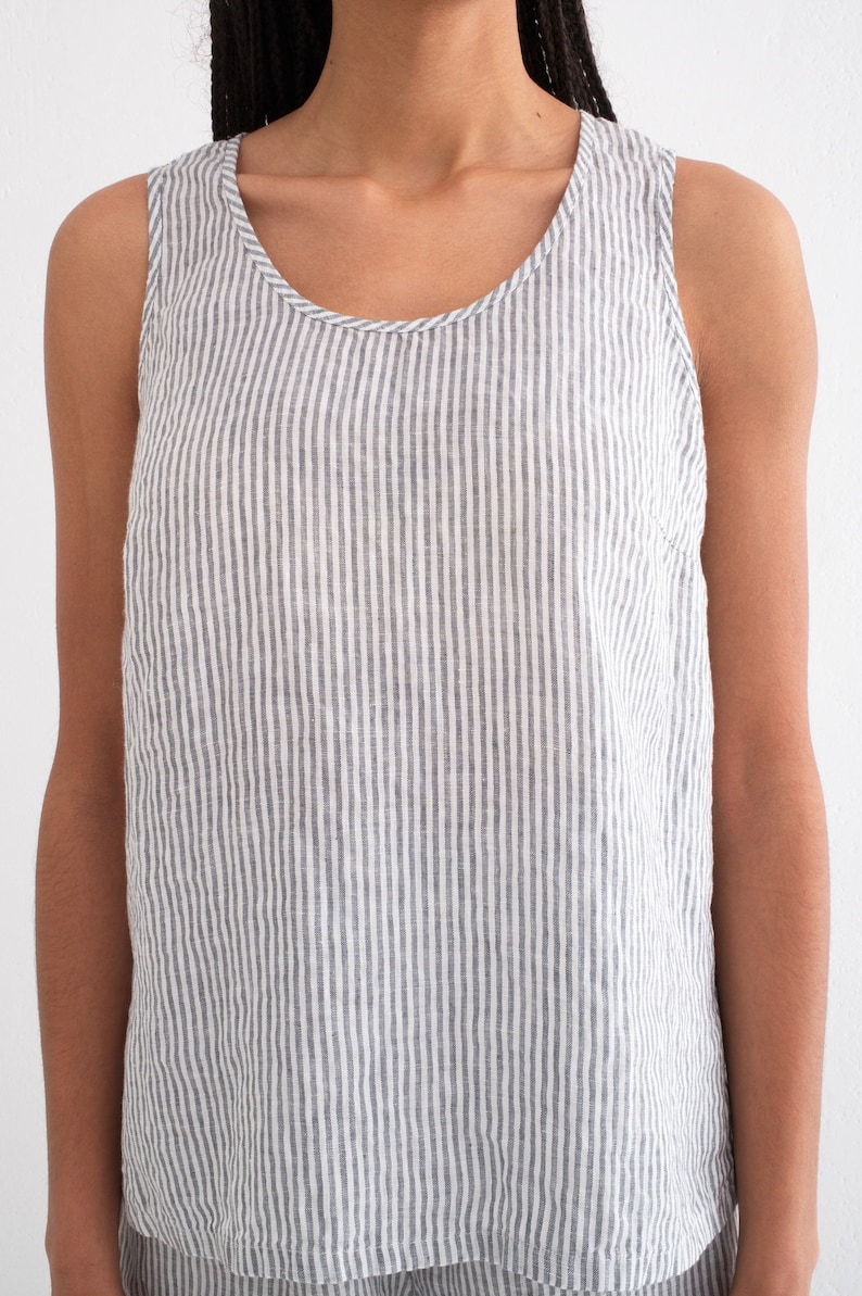 Puede incluir: Camiseta sin mangas con rayas verticales grises y blancas. La parte superior tiene un cuello redondo y est&aacute; hecha de una tela ligera. La prenda forma parte de un conjunto a juego.