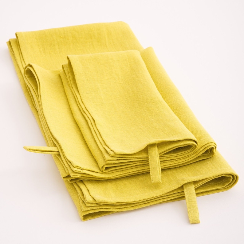 A stack of vibrant yellow linen towels, neatly folded and each featuring a hanging loop, set against a white background, highlighting their fresh and sunny color and textured weave.