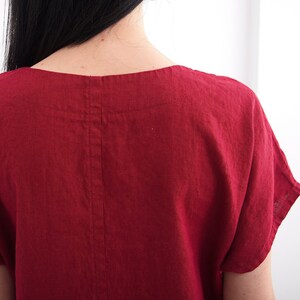 Puede incluir: Un vestido de lino rojo con un escote redondo simple y mangas cortas. El vestido tiene una costura en la espalda.