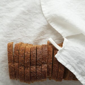 May include: A close-up of a loaf of sliced bread on a white linen tablecloth. The bread is brown and has a slightly grainy texture.