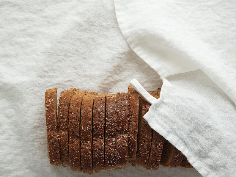 May include: A close-up of a loaf of sliced bread on a white linen tablecloth. The bread is brown and has a slightly grainy texture.