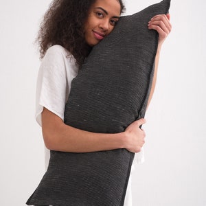 Puede incluir: Una persona sostiene una almohada a rayas blancas y negras. La almohada est&aacute; hecha de una tela suave y texturizada.