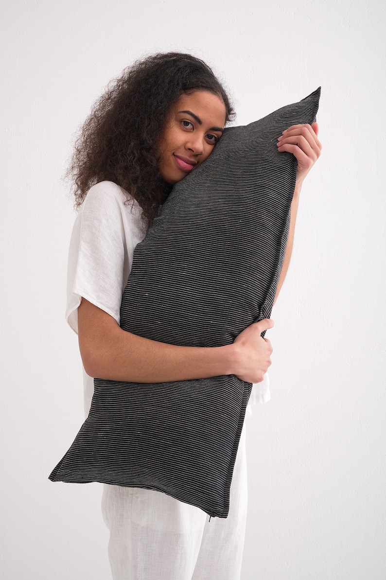 Puede incluir: Una persona sostiene una almohada a rayas blancas y negras. La almohada est&aacute; hecha de una tela suave y texturizada.
