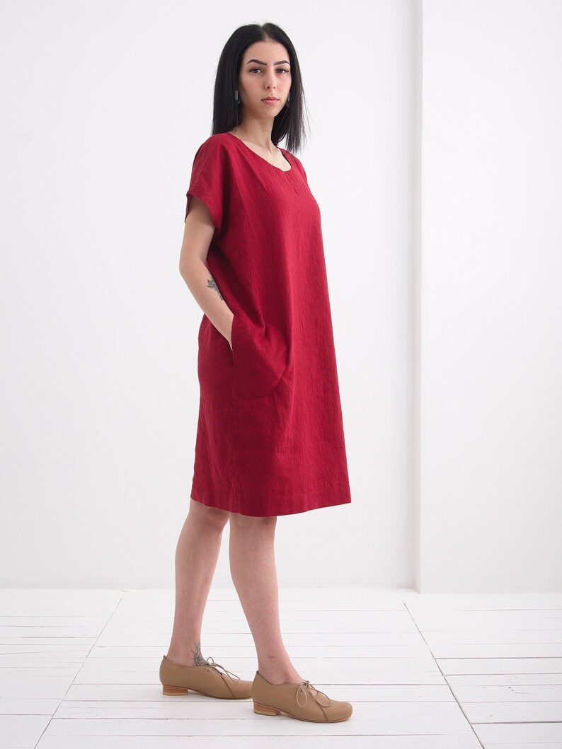 Puede incluir: Un vestido de lino rojo con mangas cortas y cuello redondo. El vestido tiene un corte holgado y llega a la mitad del muslo.