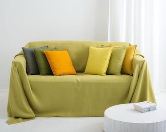 May include: A lime green sofa covered with a matching throw blanket, featuring six square throw pillows in shades of dark grey, olive green, bright orange, lemon yellow, light green, and mustard yellow, arranged across the seat cushions.