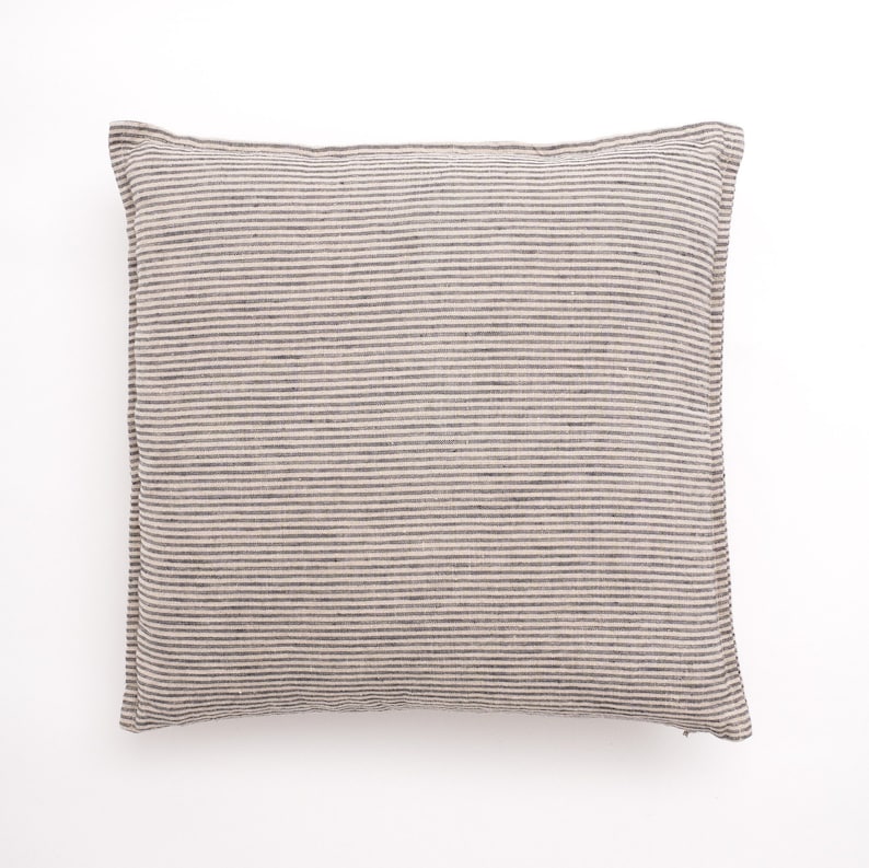 Puede incluir: Una almohada cuadrada a rayas con fondo beige y finas rayas grises oscuras. La almohada est&aacute; hecha de una tela suave y texturizada.