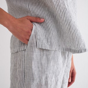Puede incluir: Conjunto de lino a rayas grises y blancas de dos piezas. La parte superior tiene un dobladillo acampanado y los pantalones cortos tienen un bolsillo. La tela tiene rayas verticales. El conjunto es informal y c&oacute;modo.