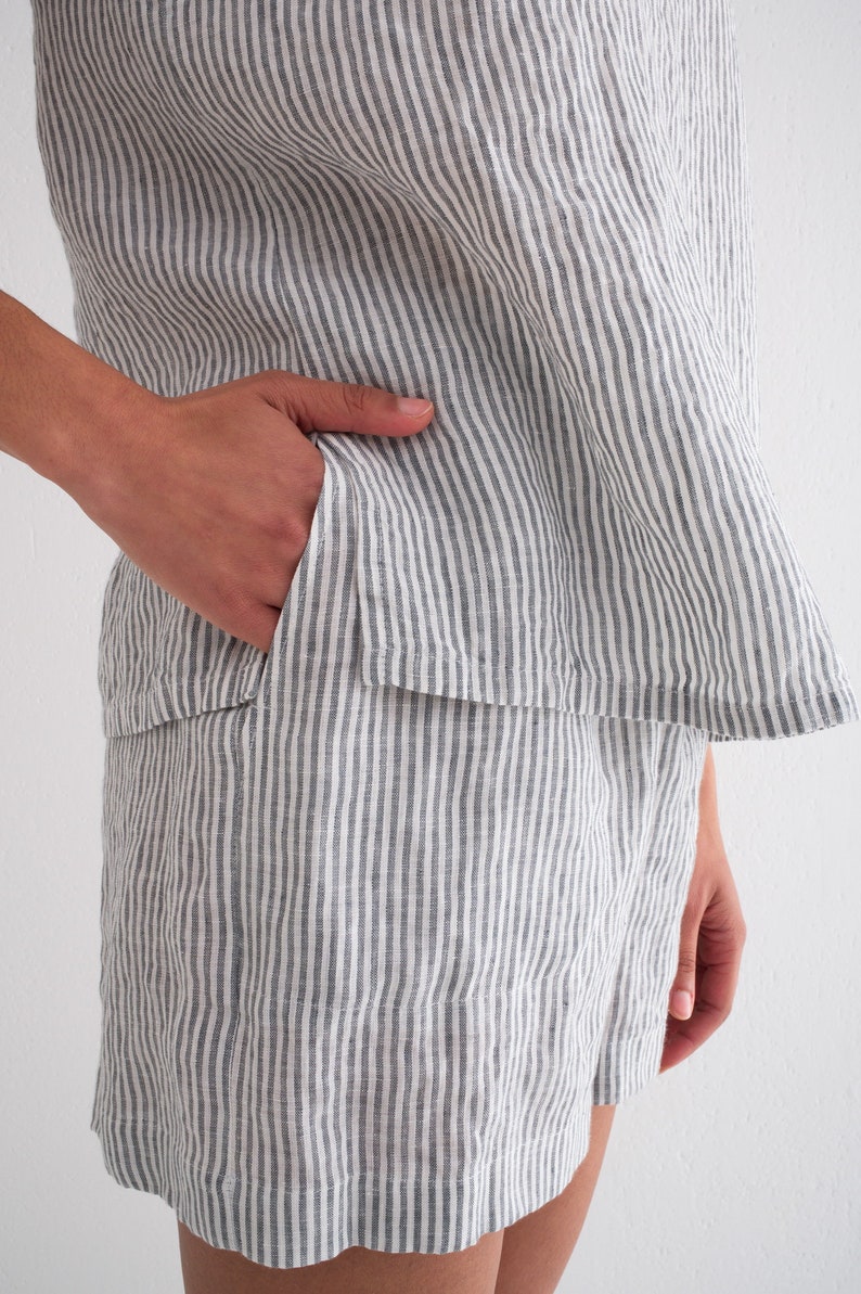 Puede incluir: Conjunto de lino a rayas grises y blancas de dos piezas. La parte superior tiene un dobladillo acampanado y los pantalones cortos tienen un bolsillo. La tela tiene rayas verticales. El conjunto es informal y c&oacute;modo.