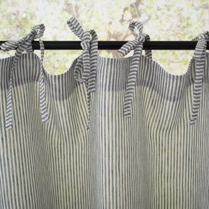 Close-up of light filtering striped linen cafe curtains with bow ties on a rod, in a country-style kitchen setting.