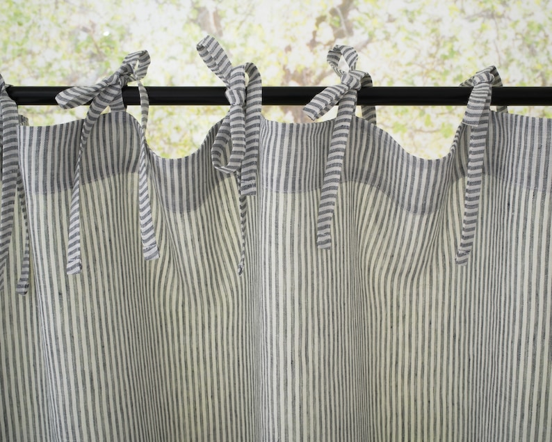 Close-up of light filtering striped linen cafe curtains with bow ties on a rod, in a country-style kitchen setting.