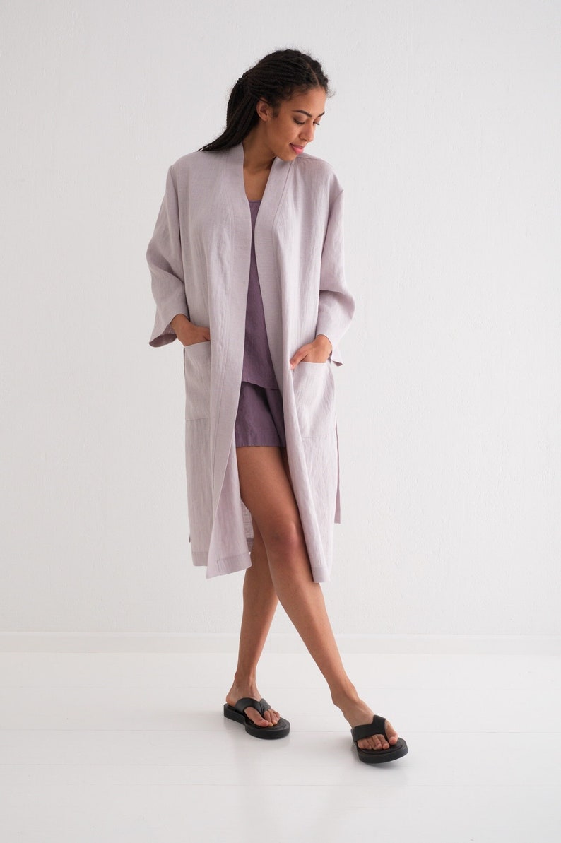 May include: A light purple linen robe with long sleeves and pockets. The robe is open in the front and the model is wearing it over a matching linen top and shorts.