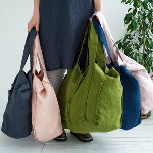 May include: Four large tote bags made of linen fabric in different colors: dark blue, light pink, green, and navy blue. The bags have a simple design with wide straps and a roomy interior.