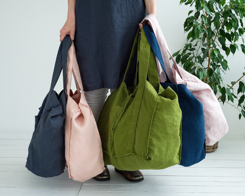 May include: Four large tote bags made of linen fabric in different colors: dark blue, light pink, green, and navy blue. The bags have a simple design with wide straps and a roomy interior.