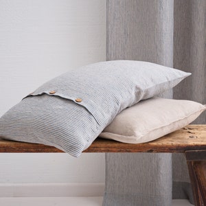 Peut inclure: Deux coussins en lin ray&eacute;s, l'un bleu et blanc, l'autre en lin naturel, sont empil&eacute;s sur un banc en bois. Le coussin bleu et blanc a deux boutons en bois.