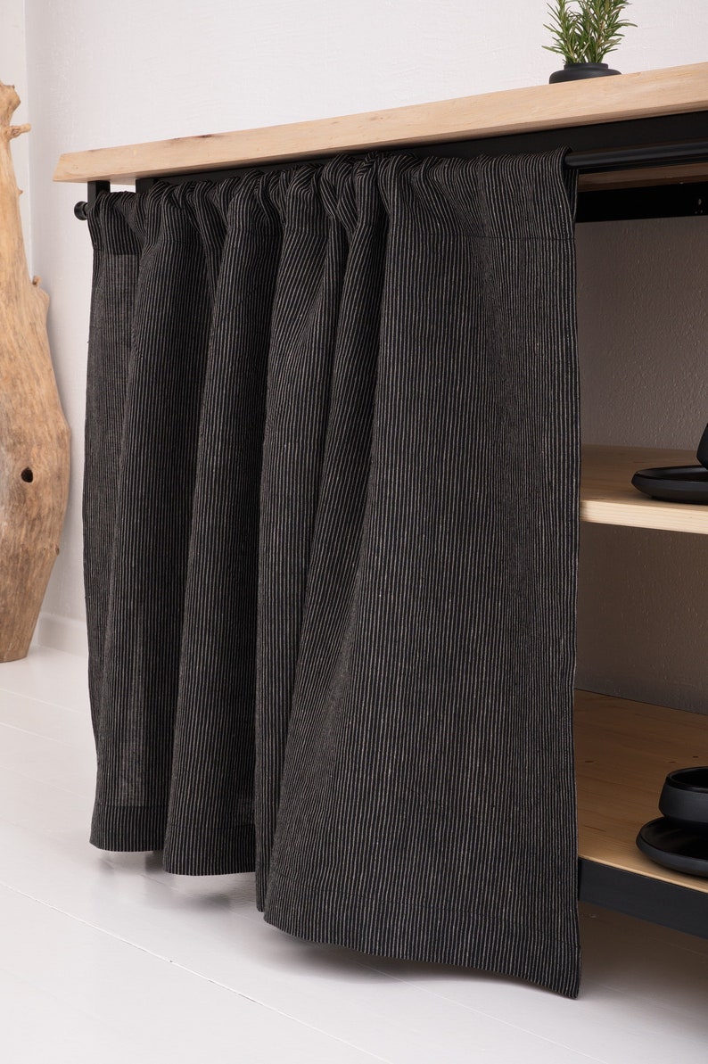 May include: Black and white striped linen curtains hanging from a wooden shelf with black metal brackets. The curtains are pulled closed, covering a shelf unit.