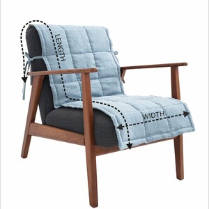May include: A modern armchair with a light blue quilted seat cover. The chair has a dark gray seat and back, with wooden armrests and legs. The seat cover is designed to fit the chair's length and width.