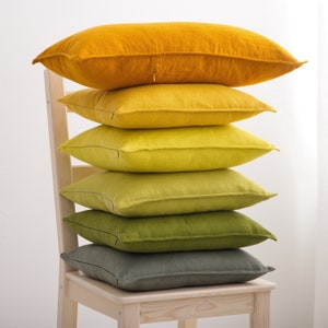 "A stack of soft linen cushions in varying shades of yellow and green, artistically placed on a wooden chair, adding a touch of natural elegance to home decor."
