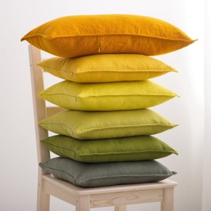 "A stack of soft linen cushions in varying shades of yellow and green, artistically placed on a wooden chair, adding a touch of natural elegance to home decor."