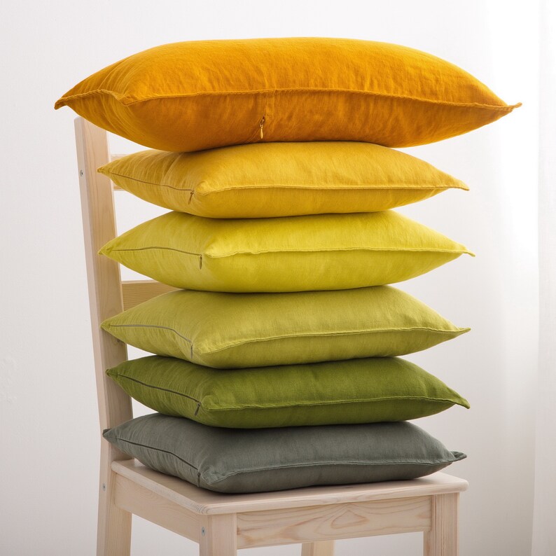 "A stack of soft linen cushions in varying shades of yellow and green, artistically placed on a wooden chair, adding a touch of natural elegance to home decor."