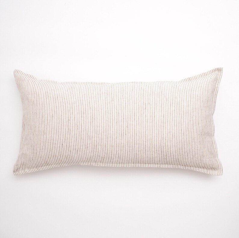 Puede incluir: Una almohada larga y rectangular con un patr&oacute;n de rayas marrones y blancas. La almohada est&aacute; hecha de una tela suave de lino.